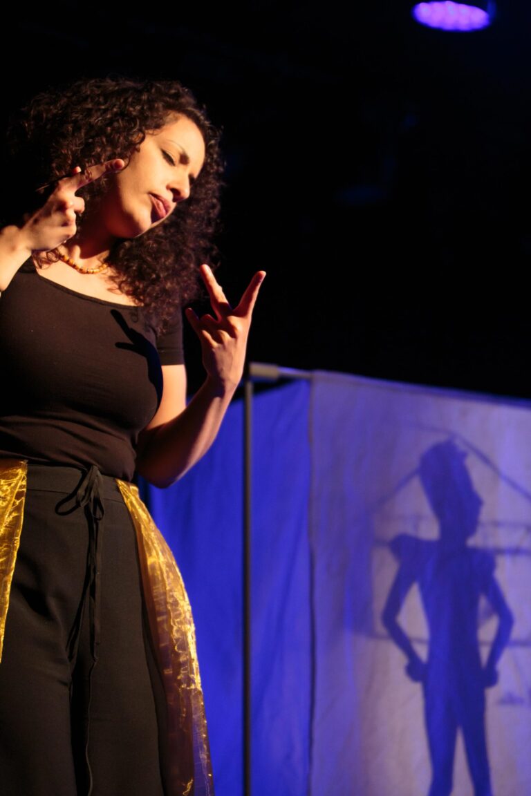 British Sign Language Interpreter Sumayya Si-Tayeb signing in front of the shadow puppetry screen with a figure of a man in uniform